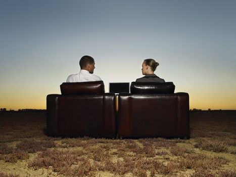 Rear view of business people sitting on leather chairs in open plain at sunset
