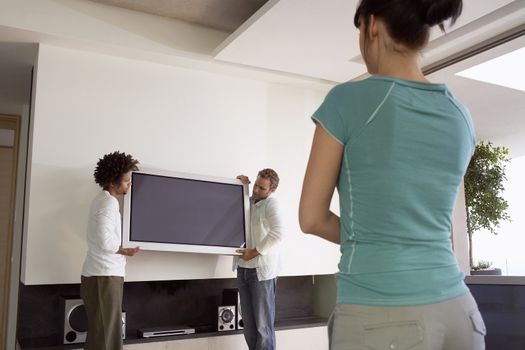 Young woman watching two men moving plasma television into new house