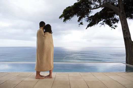 Side view of young couple wrapped in blanket looking at infinity pool