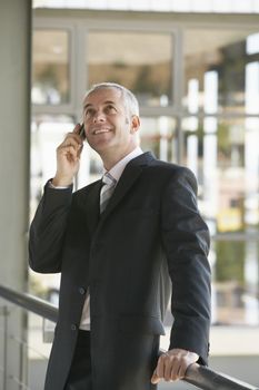 Happy middle aged businessman using cell phone while looking up in office