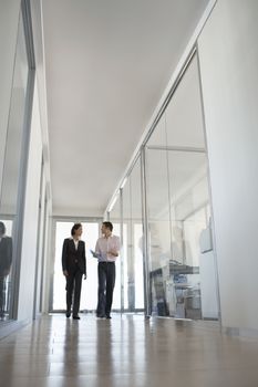 Two business people walking while talking in hallway