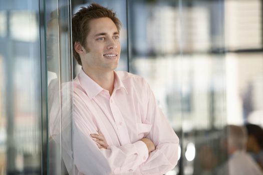 Happy businessman with arms crossed leaning on office glass door