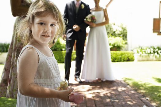 Portrait of a cute girl holding flower petals with bride and groom standing in background