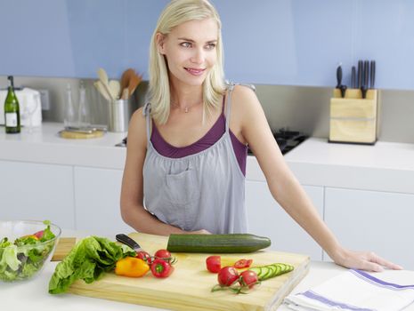 Young woman standing at kitchen counter with freshly cut vegetable on chopping board