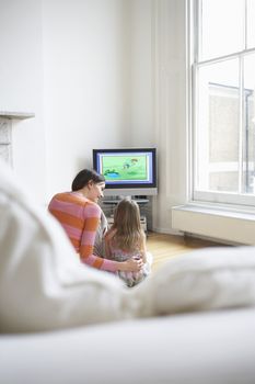Rear view of mother and daughter watching cartoons in television at home