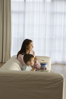 Side view of mother and son watching television while eating icecream at home