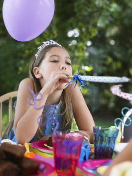 Young girl blowing party puffer at outdoor birthday party