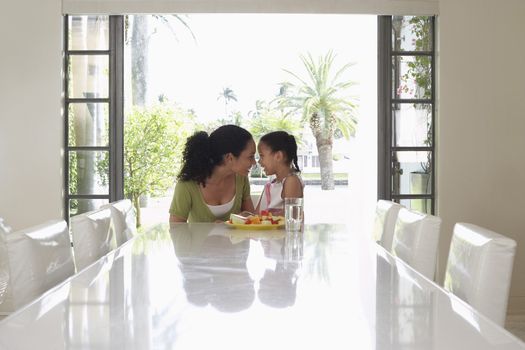 Playful mother and daughter sitting at dining table