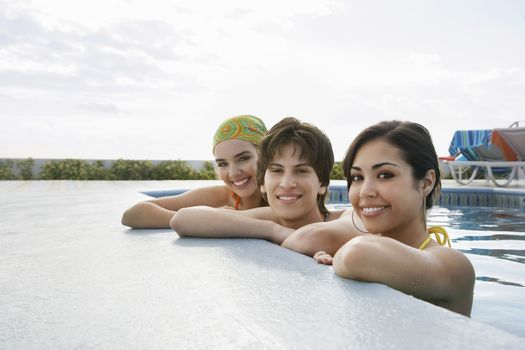 Portrait of teenage boy with female friends resting at the edge of swimming pool