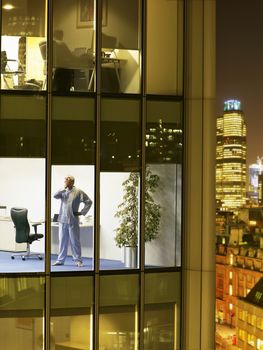 Man wearing pajamas standing in office and yawning view from building exterior