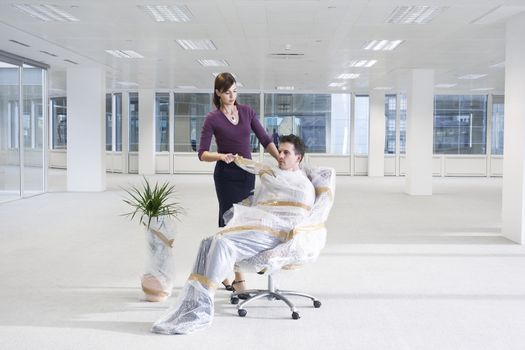 Secretary unwrapping businessman on chair in empty office space