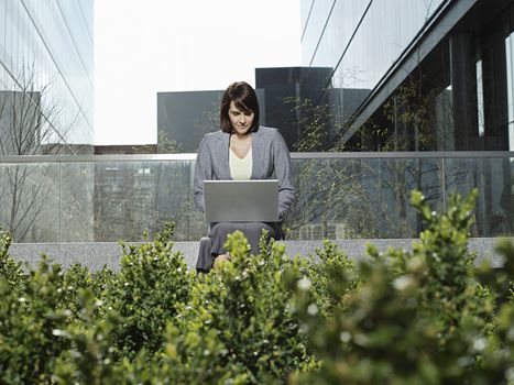 Young businesswoman using laptop outside office buildings