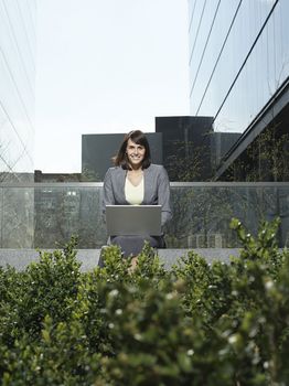 Portrait of happy young businesswoman using laptop outside office buildings