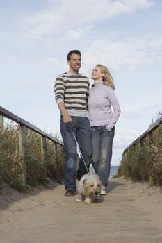 Happy couple walking with dog on boardwalk at beach