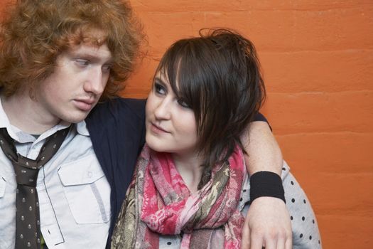 Closeup of young couple with arm around looking at each other against orange brick wall