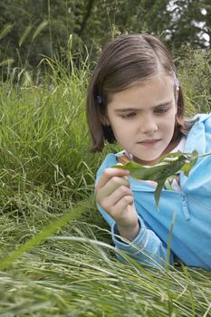 Cute young girl examining caterpillar on leaf outdoors