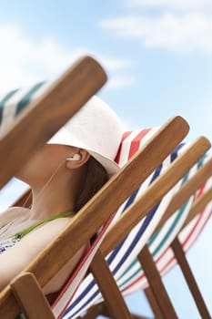Closeup of woman listening music through earphones on deckchair at beach