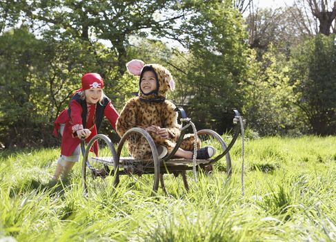 Young boy in pirate costume pushing smiling boy in jaguar costume on cart in the garden