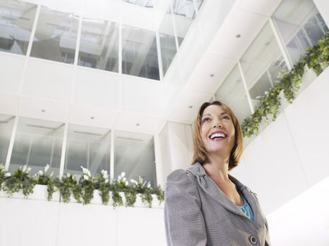 Smiling businesswoman standing in atrium of office building low angle view