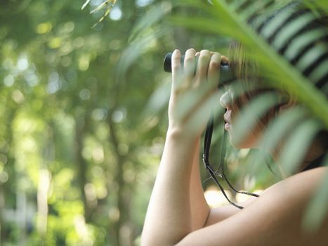 Side view of a young woman using binoculars in tropical forest