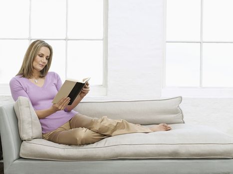 Mid adult woman reading book on sofa