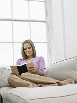 Mid adult woman reading book on sofa