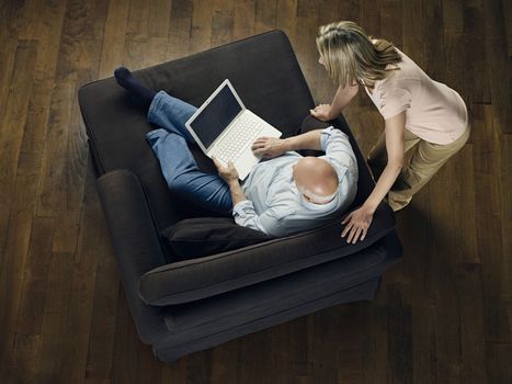 Top view of a woman watching mature bald man use laptop on sofa at home