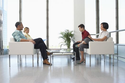 Full length side view of four business people sitting in modern waiting room at office