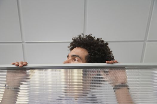 Young male office worker peering over cubicle wall in the office