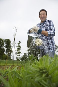 Low angle view of a smiling man watering crops in field against clear sky