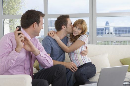 Male real estate agent using mobile phone as couple kiss by in new home