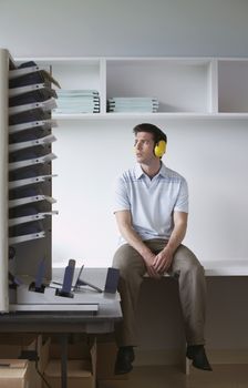 Full length of a man with ear protectors sitting by photocopier in office