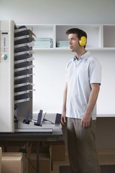 Side view of a man with headphones standing by photocopier in office