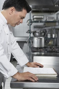 Side view of a middle aged male chef reading recipe book in the kitchen