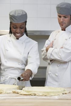 Male chef watching female colleague prepare food in the kitchen