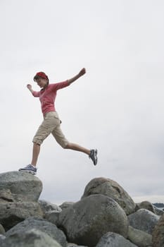 Woman with arms outstretched jumping on rocks
