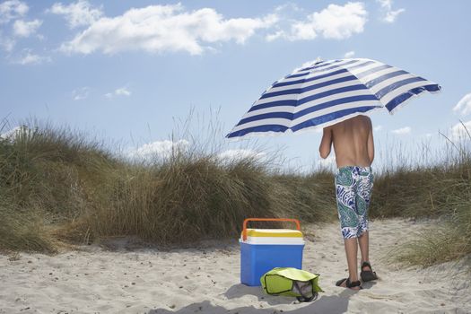 Full length rear view of a boy standing on beach under umbrella