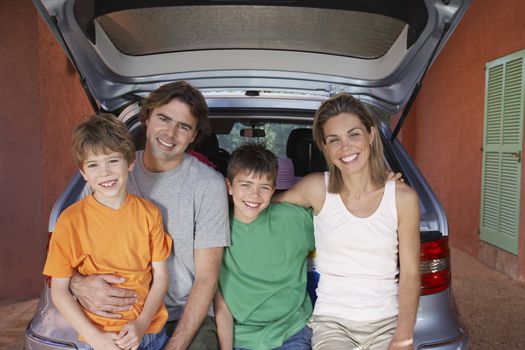 Portrait of a happy couple with two sons sitting on car tailgate