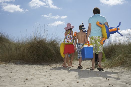 Full length rear view of parents and three children carrying beach accessories on shore