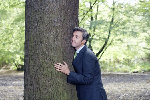 Businessman with eyes closed embracing tree trunk in forest