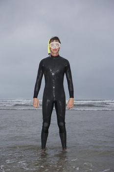 Man in wetsuit wearing snorkle standing in water on beach portrait