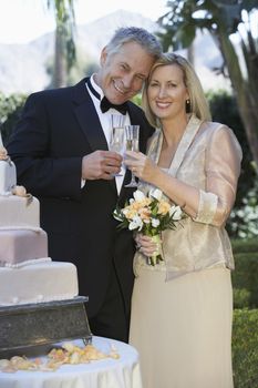 Portrait of happy couple toasting champagne flutes near wedding cake