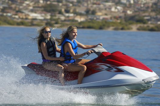 Two young women riding personal watercraft on lake