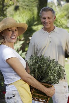 Portrait of a senior woman holding potted plant with man standing in the background