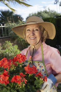 Portrait of a happy senior woman in straw hat holding flower plant