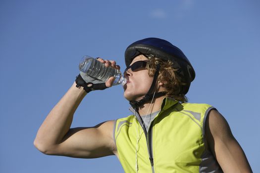 Young male bicyclist drinking water from bottle against blue sky