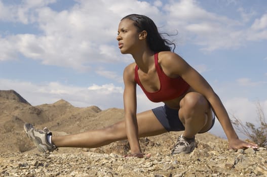 Mixed race female jogger stretching in mountains against cloudy sky