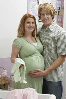 Portrait of an expectant couple with baby clothes in bedroom