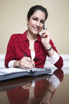 Business woman using mobile phone and writing in diary