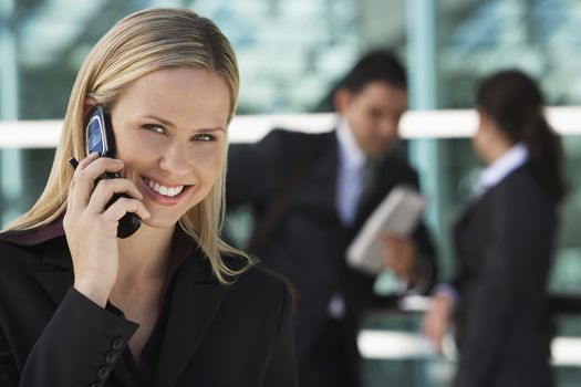 Portrait of a happy businesswoman using cell phone with colleagues in background
